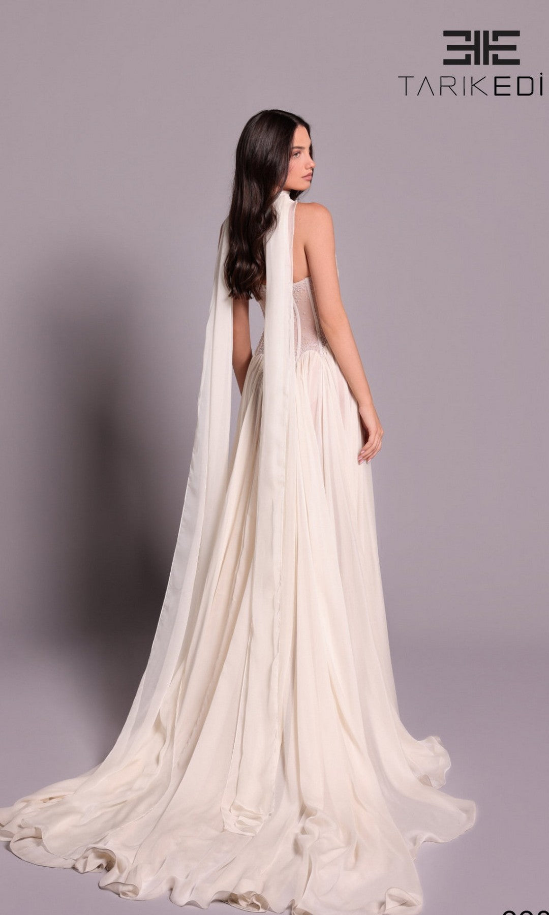 A woman in the Long Formal Dress: Tarik Ediz 99076, featuring a flowing chiffon skirt, stands facing away against a plain background.